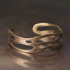 Close up of a vintage copper open cuff bracelet with curved cutout details on a dark surface
