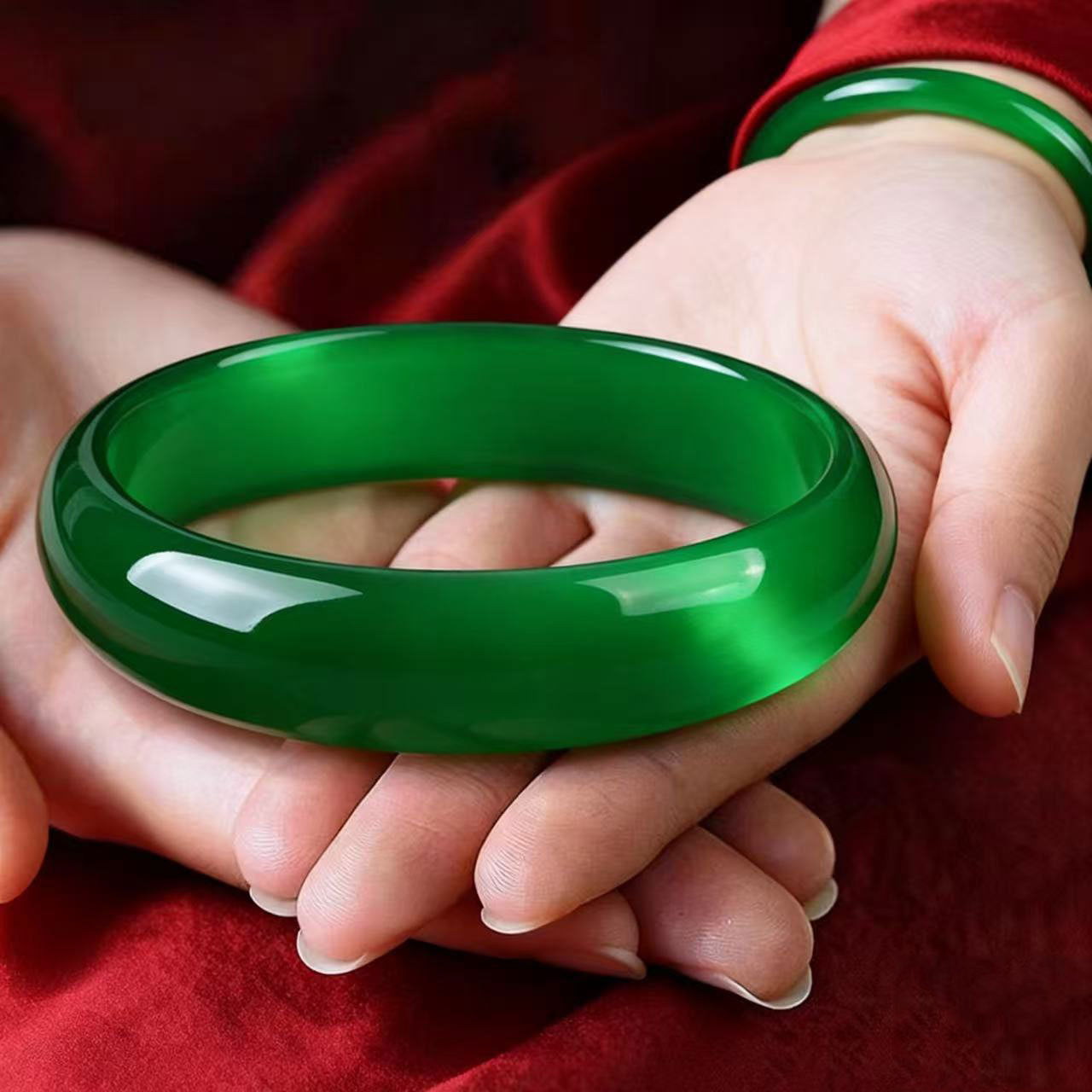 A wide deep green cat's eye glass bangle bracelet held in hands against a red background