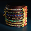 Stack of colorful hand-woven bracelets with gold-tone beads on a dark cylinder stand