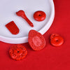 Assortment of carved red cinnabar charms including pendants and beads on a white plate