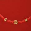 Close-up of a red braided bracelet with a gold Fu character charm against a red background