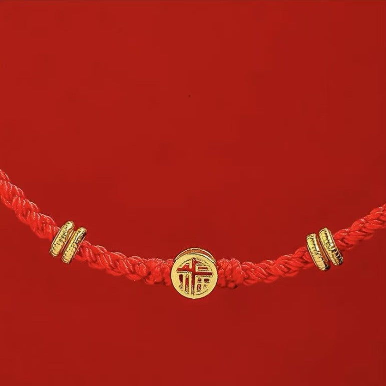 Close-up of a red braided bracelet with a gold Fu character charm against a red background