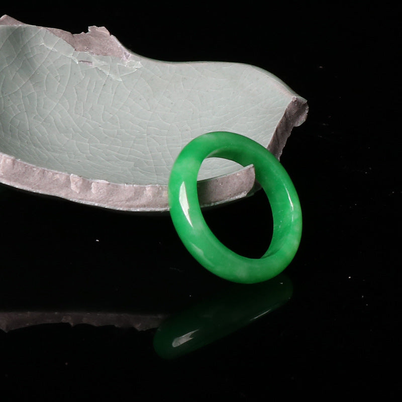 A smooth, vibrant green natural jade ring resting on a textured ceramic dish.