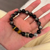Hand wearing a black beaded bracelet with a mantra charm