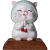 White ceramic cat figurine with green scarf and praying hands on wooden base