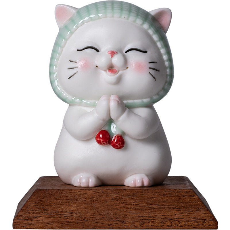 White ceramic cat figurine with green scarf and praying hands on wooden base