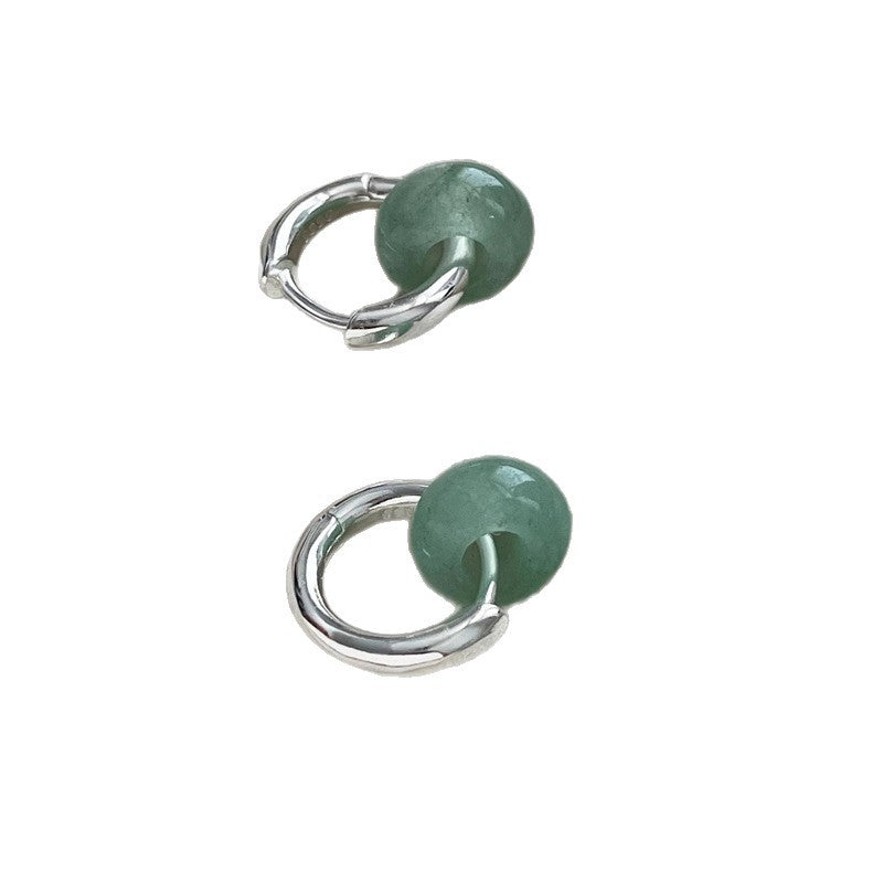 Close-up of a silver hoop earring with a round green stone pendant on an ear
