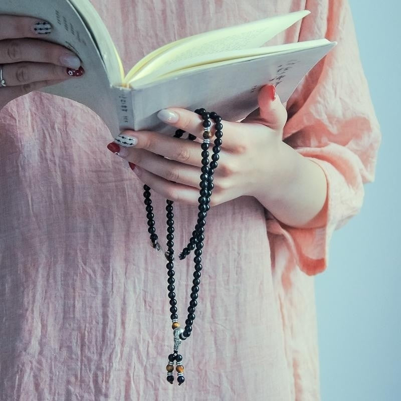 Hands holding a book while wearing a long black agate and tiger eye mala bracelet