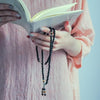 Hands holding a book while wearing a long black agate and tiger eye mala bracelet