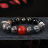 Close up of a beaded bracelet with black obsidian, speckled stones and a red carved center bead