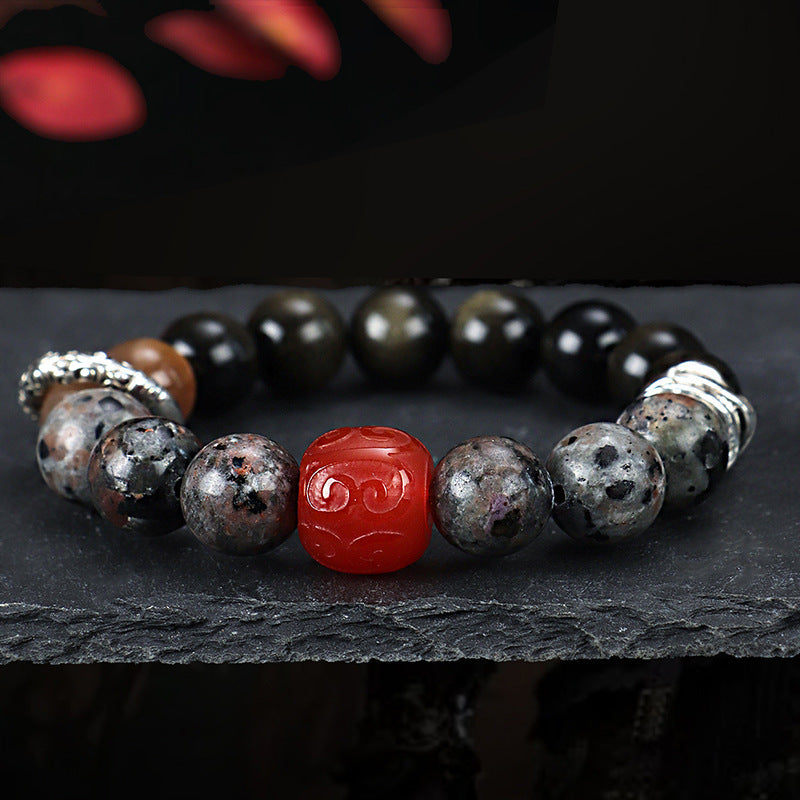 Close up of a beaded bracelet with black obsidian, speckled stones and a red carved center bead