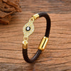 Close up of a braided brown leather bracelet with a gold tone evil eye charm set with clear stones
