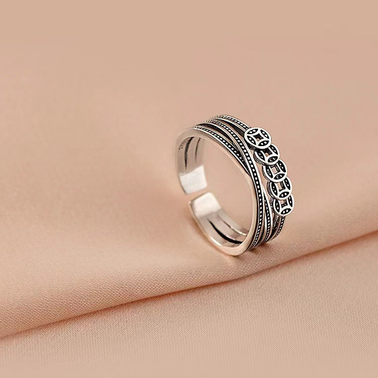 Close up of a silver tone adjustable ring with five coin charms on a soft fabric background