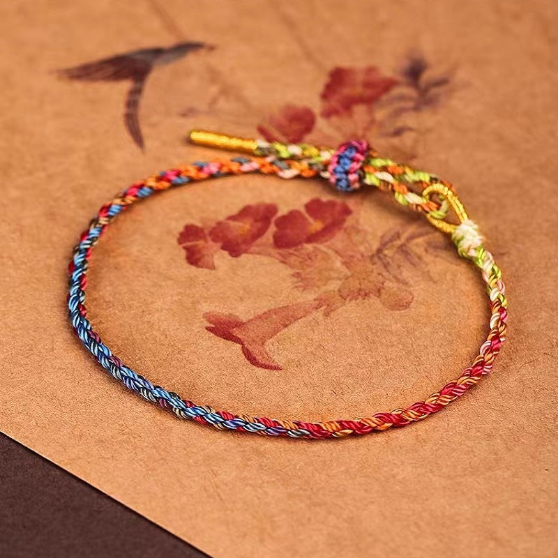 Close-up of a multicolored braided rope bracelet with a gold-tone clasp on a textured brown background.