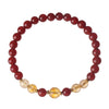 Close up of a red agate and yellow citrine beaded bracelet on a textured surface
