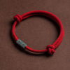 Close-up of a red cord rope bracelet with a central bead and knotted ends on a brown background