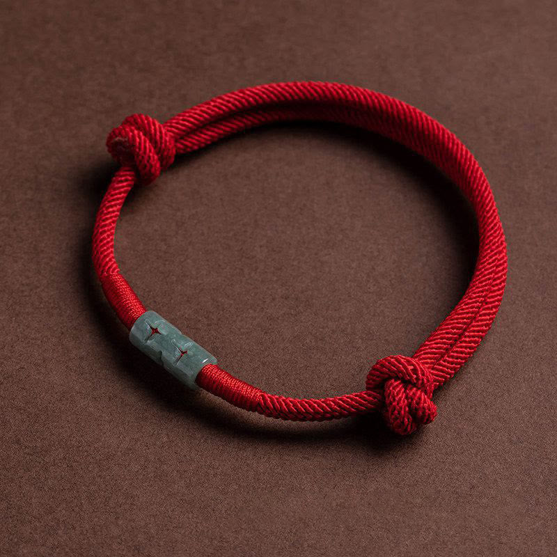 Close-up of a red cord rope bracelet with a central bead and knotted ends on a brown background