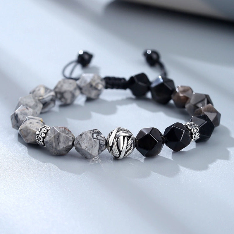 Close up of a bracelet with black and grey faceted beads and a silver leaf charm on a white surface