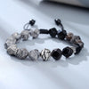 Close up of a bracelet with black and grey faceted beads and a silver leaf charm on a white surface
