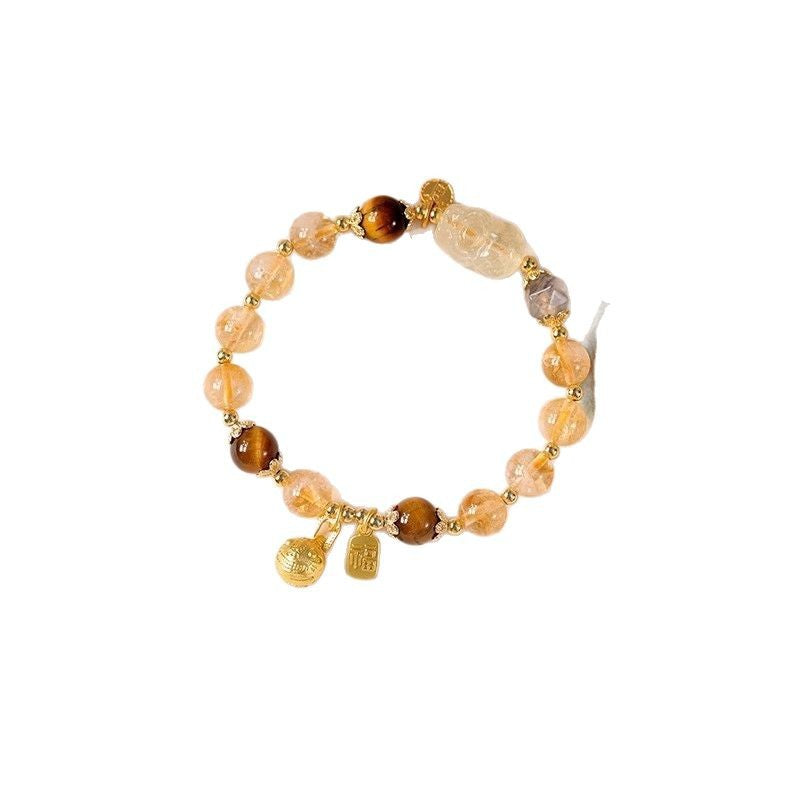 Close-up of a beaded bracelet with yellow citrine, brown tiger eye, and a carved pixiu charm.