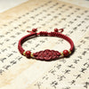 Close-up of a red woven bracelet with a cinnabar coin charm on a background of calligraphy