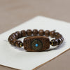 Close-up of a dark brown agarwood bracelet with a carved rectangular charm and blue center stone