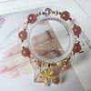 Pink strawberry quartz beaded bracelet with a gold butterfly charm on a clear stand