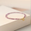 Close-up of a purple faceted amethyst bead bracelet with a gold clasp on a white box