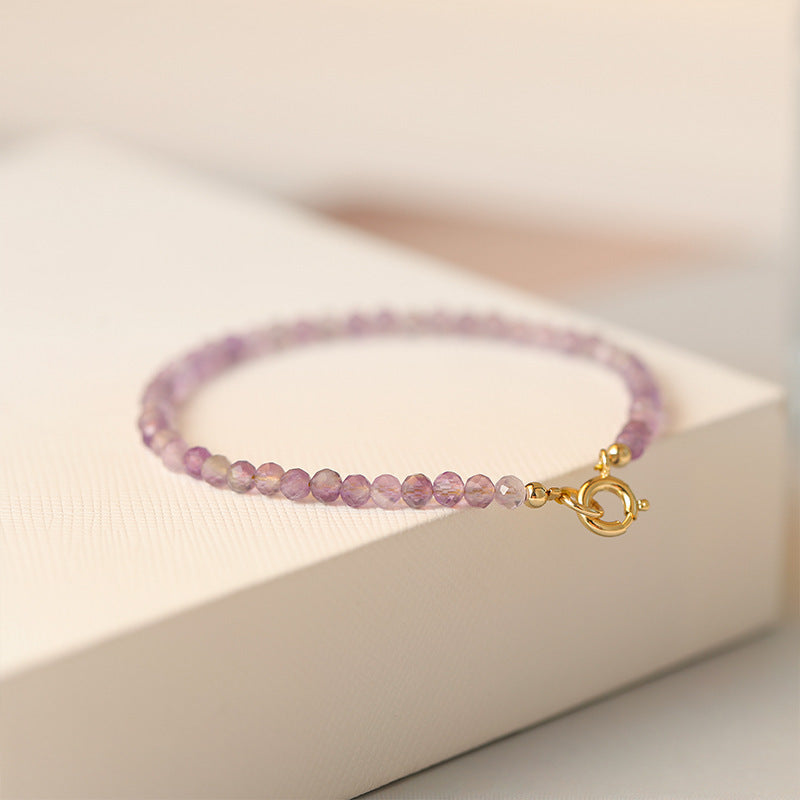 Close-up of a purple faceted amethyst bead bracelet with a gold clasp on a white box