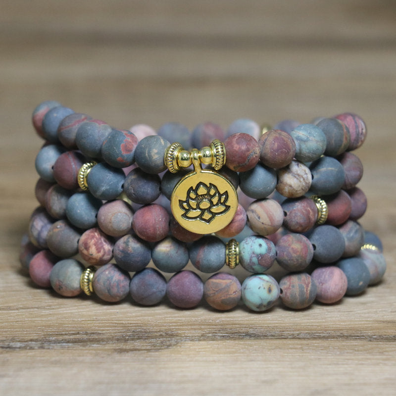 Coiled multi-strand Picasso Jasper mala bracelet with gold lotus charm on wood surface