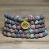 Coiled multi-strand Picasso Jasper mala bracelet with gold lotus charm on wood surface