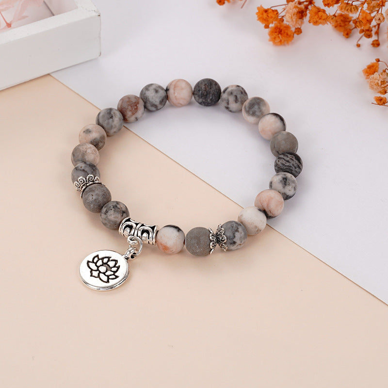 Beaded bracelet with grey and pink stones and a silver lotus charm lying on a beige surface