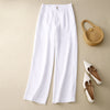Flat lay of white wide leg linen pants with a straw bag and white shoes