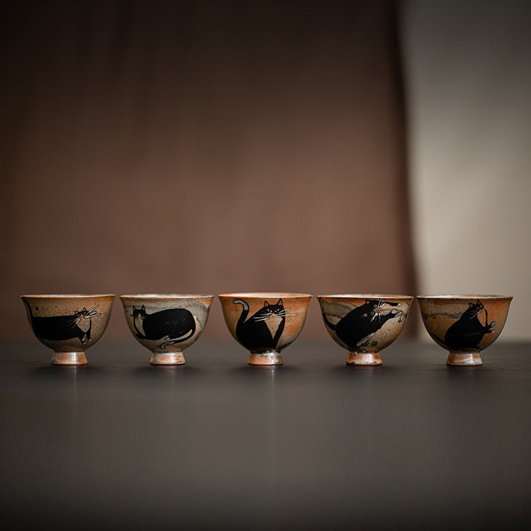 Five small ceramic tea cups with black cat designs lined up on a table