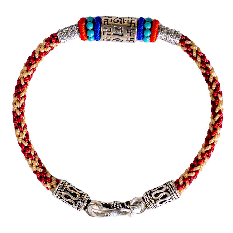 Close up view of a red and gold braided bracelet with a silver mantra cylinder