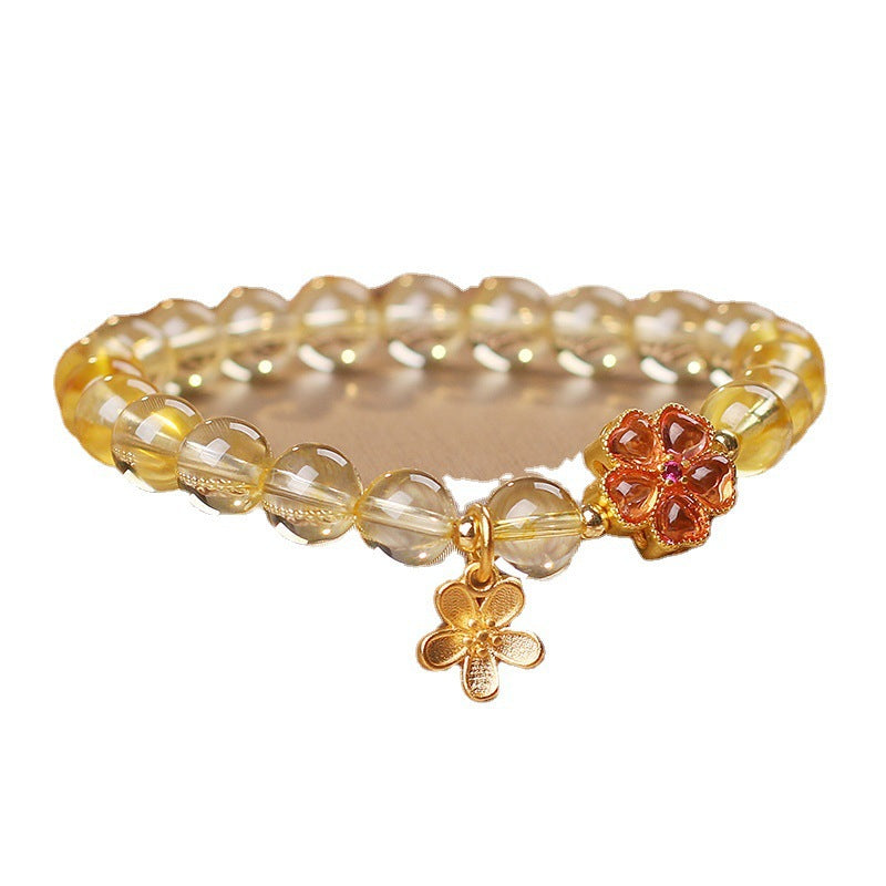 Yellow natural citrine bead bracelet with gold tone flower charm pendant on white background