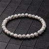 A close-up view of a white howlite beaded bracelet on a dark textured surface