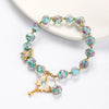 Close up of a glass bead bracelet with pink roses and a gold butterfly charm on a white surface
