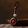 Close up of a dark wood ring keychain with a carved red cinnabar charm inside.