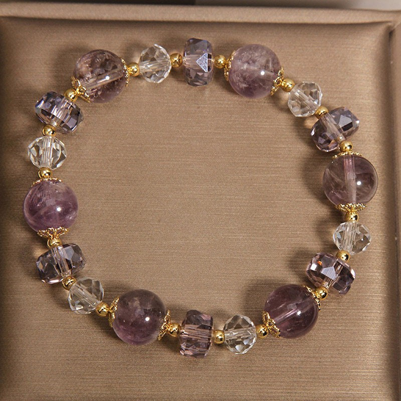 Close-up of a purple amethyst and clear crystal beaded bracelet on a beige surface