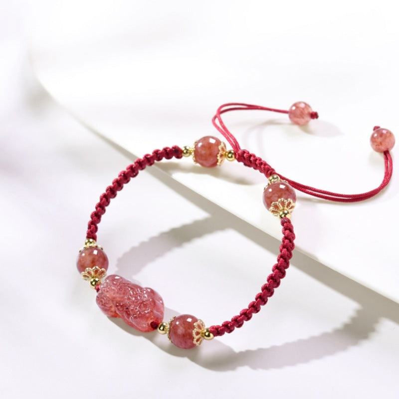 Close-up of a red braided bracelet with pink strawberry crystal beads and a carved Pixiu charm
