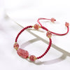 Close-up of a red braided bracelet with pink strawberry crystal beads and a carved Pixiu charm
