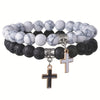 Two stacked bracelets with white marble and black lava stone beads featuring cross charms