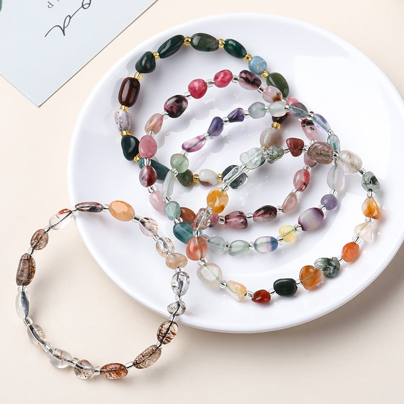 A collection of bracelets made from natural irregular shape stones in various colors displayed on a white plate.