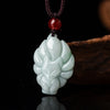 Close up of a light green carved jade nine tailed fox pendant on a dark cord