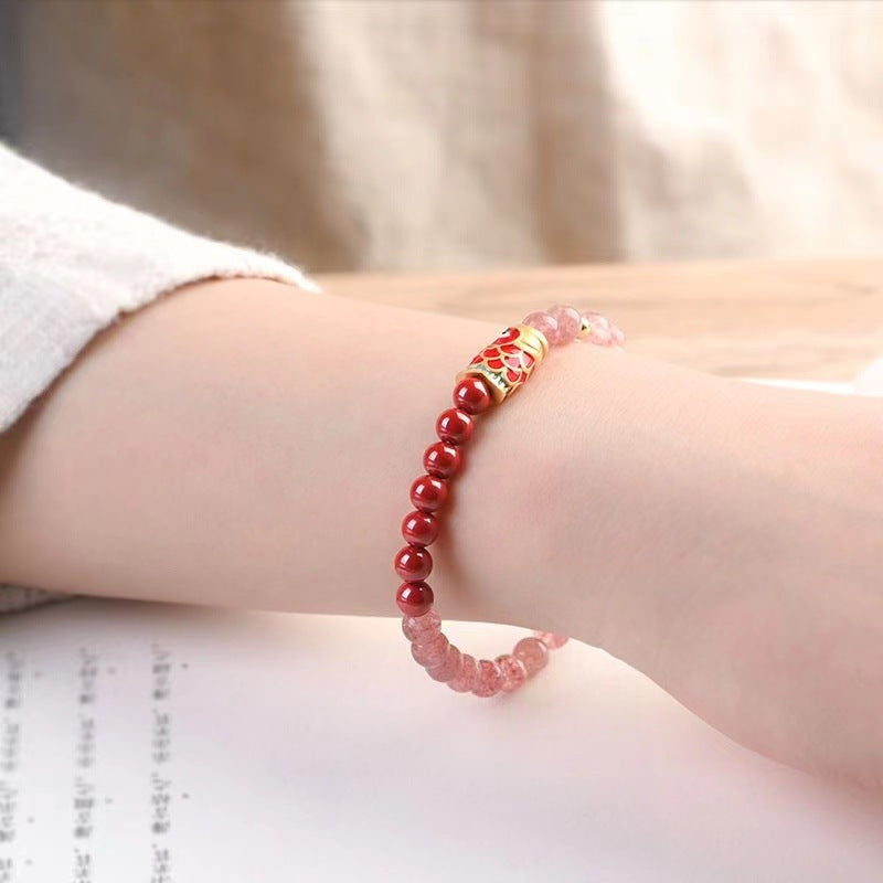 A wrist wearing a bracelet with red cinnabar beads, pink strawberry quartz beads, and a gold-tone koi fish charm.
