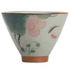 Close-up of a hand-painted ceramic teacup featuring a pink lotus flower and a koi fish on a crackled white background.