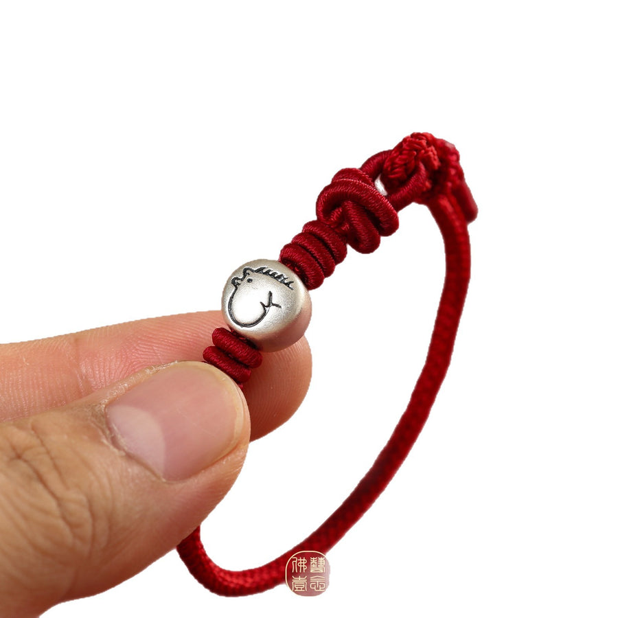 Close up of a red string bracelet with a silver rat charm held between fingers