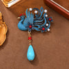 Close-up of a blue plated phoenix brooch with a hanging faux turquoise stone