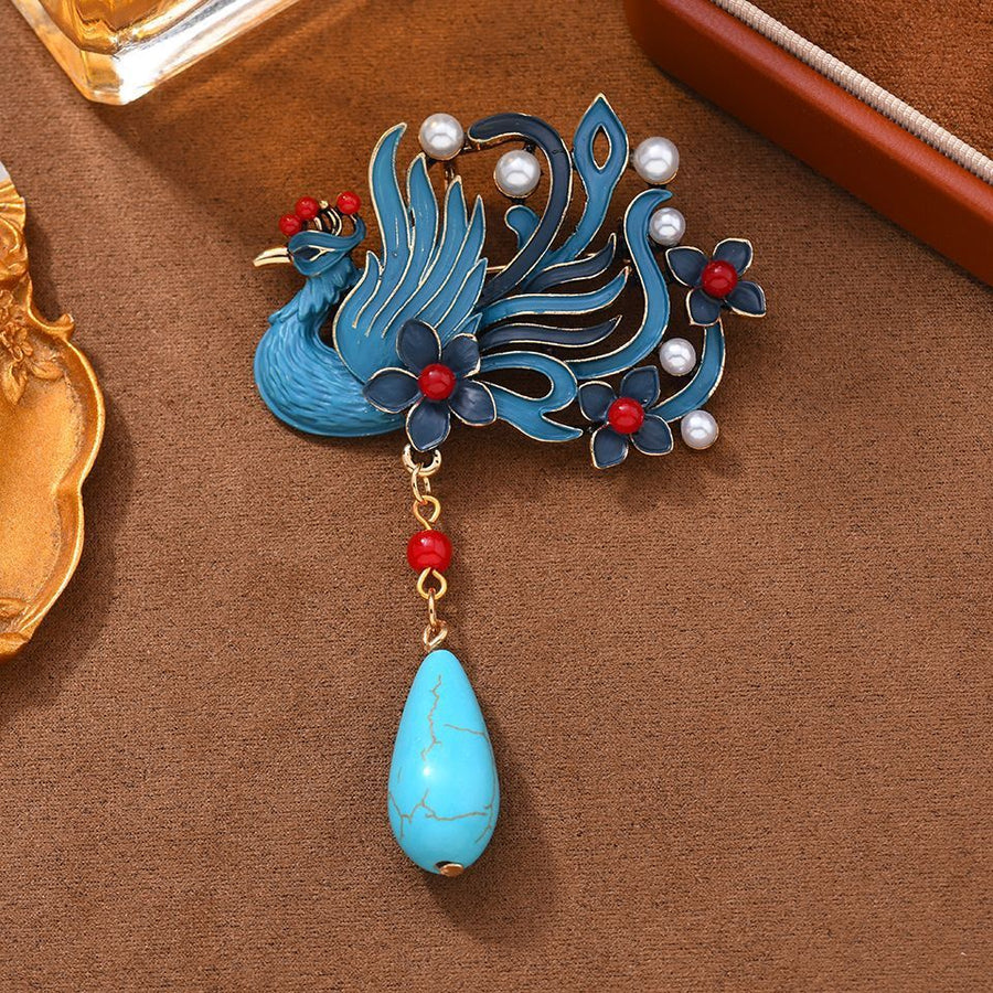 Close-up of a blue plated phoenix brooch with a hanging faux turquoise stone